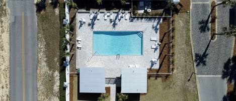 Vista aérea de un área de piscina con sillones de descanso, una alberca y un porche cubierto.