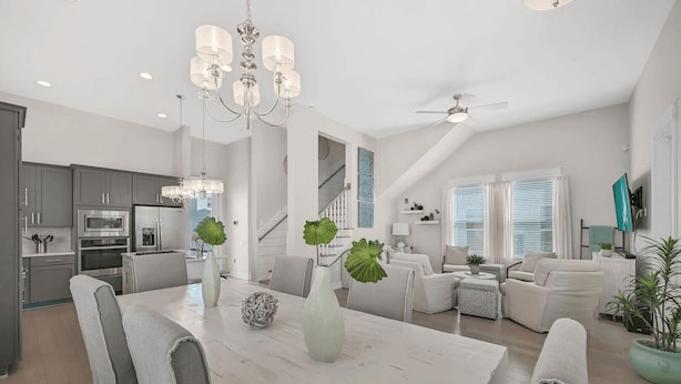 A modern kitchen with stainless steel appliances, a dining area with a white table and chairs, and a living room with a sofa and coffee table.