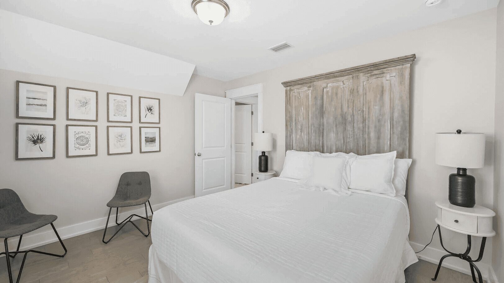 A hotel room with a large bed, a chair, a bedside table with a lamp, and framed artwork on the wall.