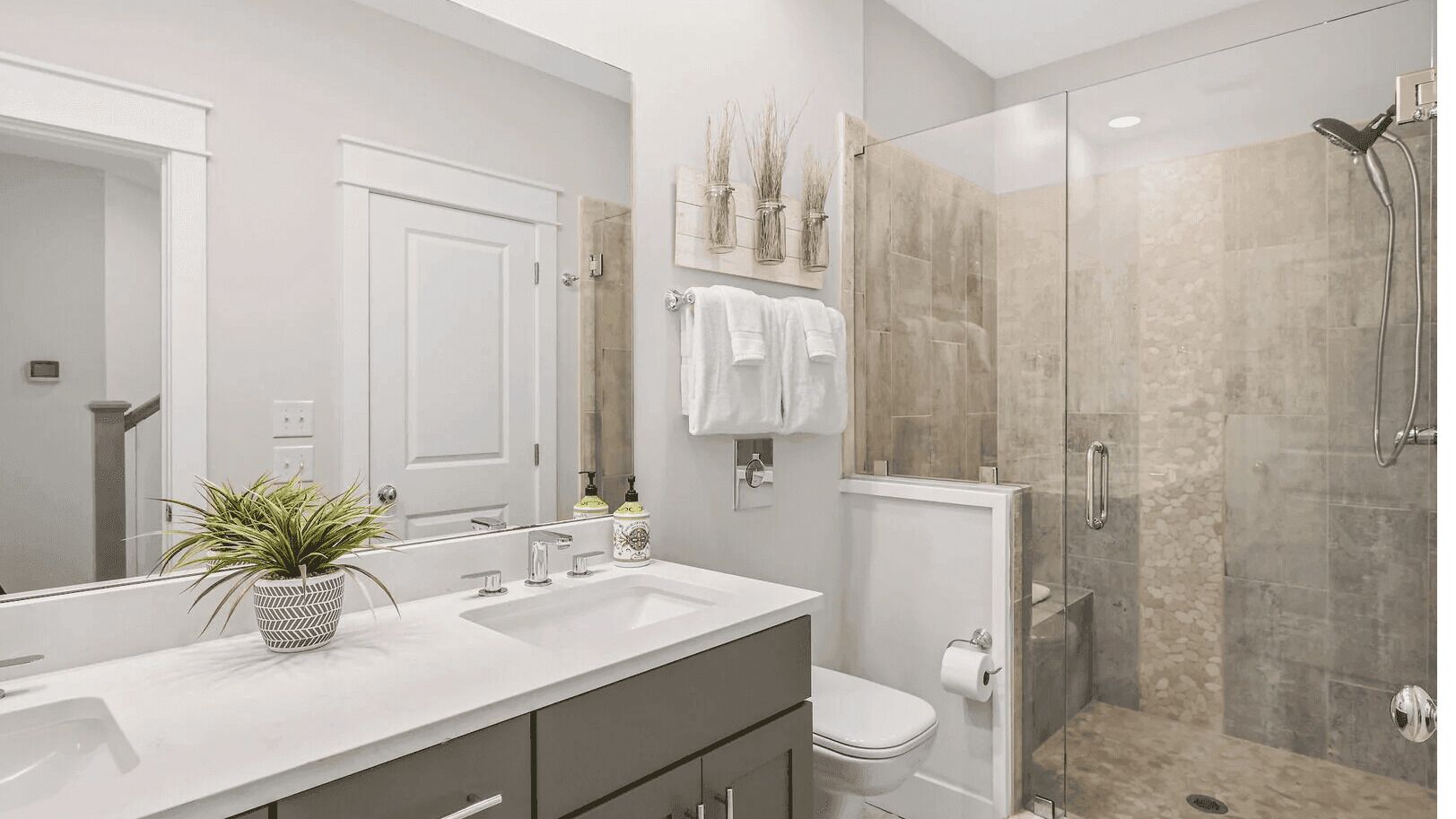 A modern bathroom with a double sink, a toilet, and a glass-enclosed shower.
