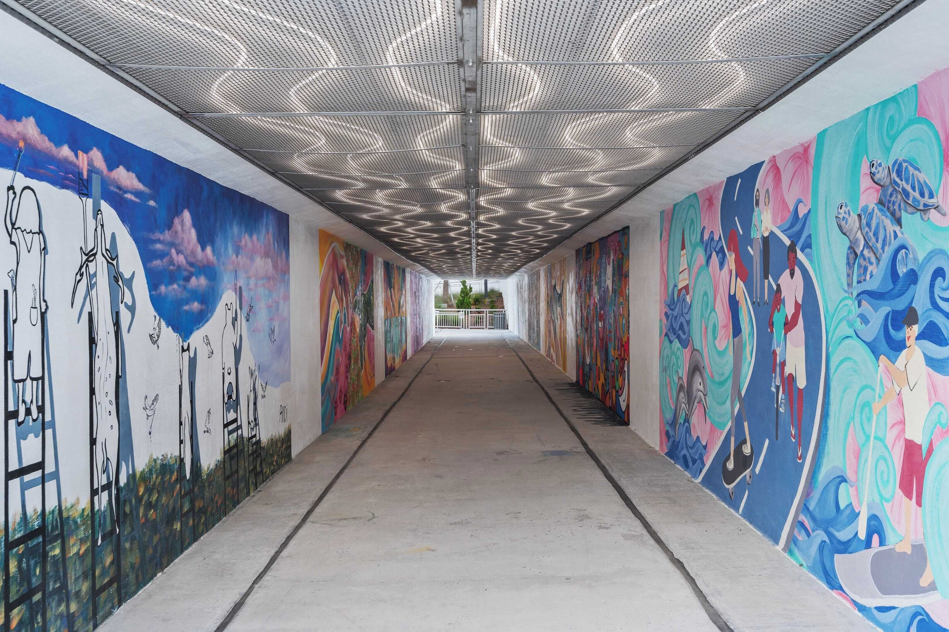 A corridor with colorful murals on the walls, a metal ceiling, and a concrete floor.