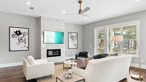 Una sala de estar moderna con un sofá blanco, un televisor de pantalla plana sobre una chimenea, y obras de arte en las paredes.