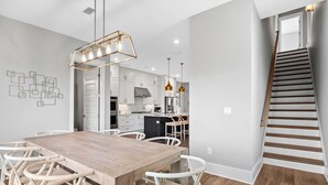 Una cocina moderna con armarios blancos, una mesa de comedor de madera y una escalera.