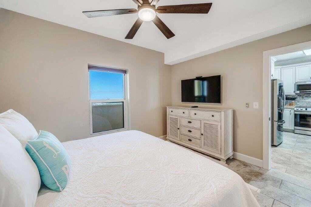 Een slaapkamer met een bed, een plafondventilator, een televisie en een raam.