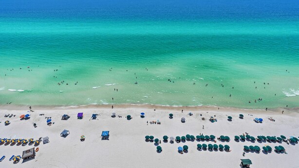 A beach with clear turquoise waters, a sandy shore, and numerous beach umbrellas and lounge chairs.