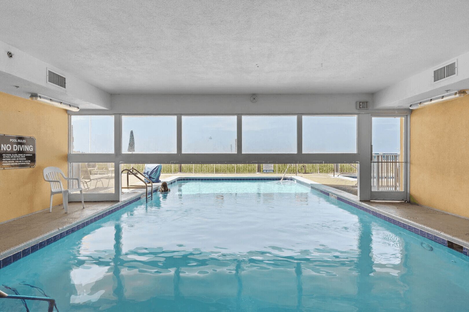 An indoor swimming pool with clear pool rules, a no diving sign, and a view of the outside.