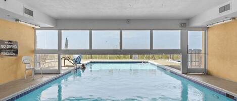 An indoor swimming pool with clear pool rules, a no diving sign, and a view of the outside.