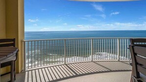 A balcony with a view of the ocean, featuring a railing and two wooden chairs.