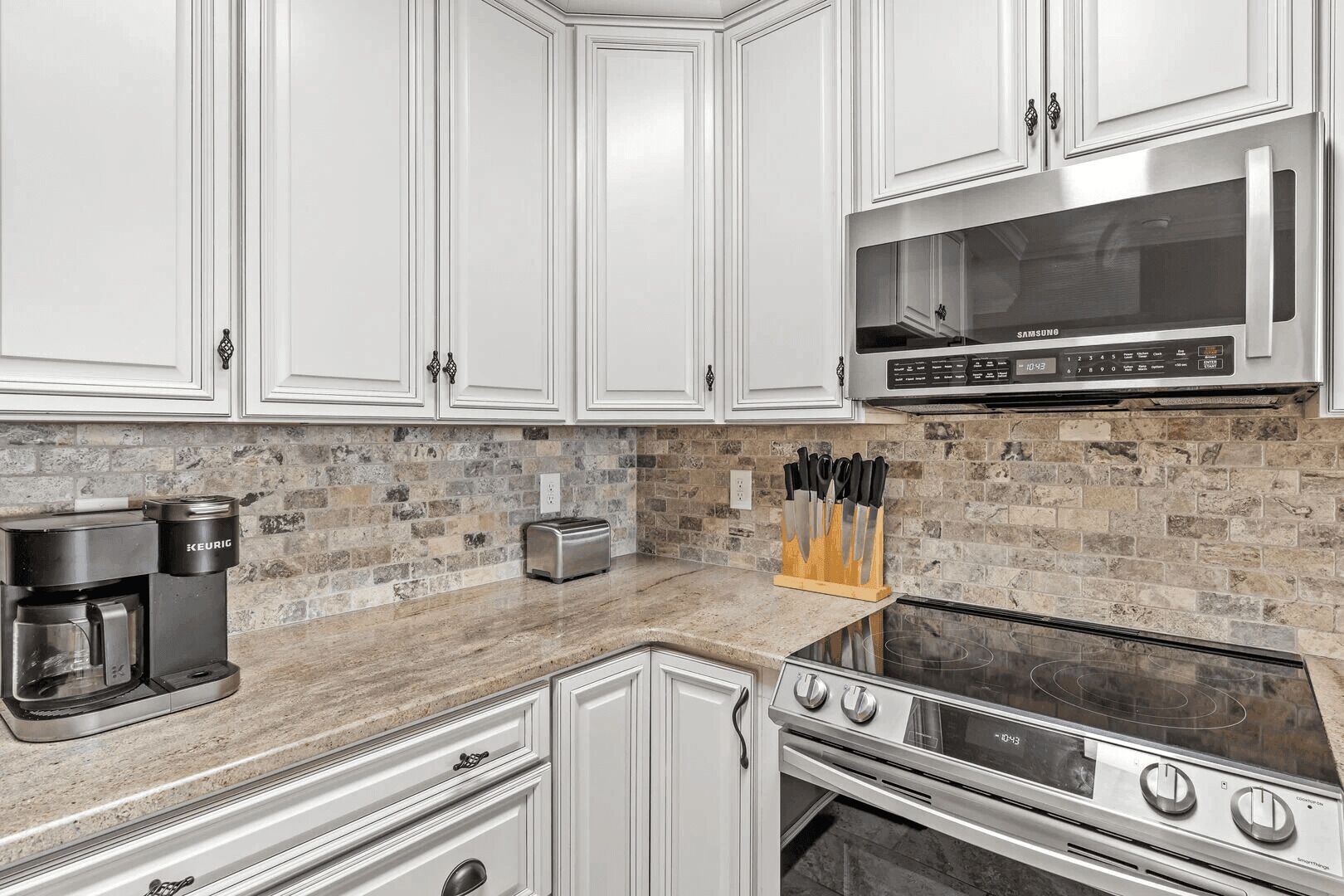 A modern kitchen with white cabinetry, a built-in microwave, a Keurig coffee maker, a toaster, and a stove.