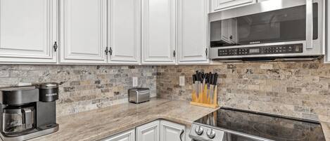 A modern kitchen with white cabinetry, a built-in microwave, a Keurig coffee maker, a toaster, and a stove.