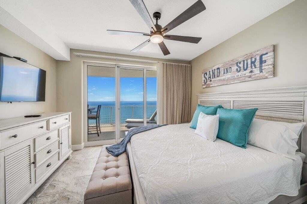 Een slaapkamer met een groot bed, een plafondventilator, een televisie, een dressoir en uitzicht op de oceaan.
