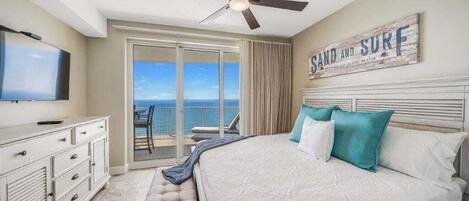 Een slaapkamer met een groot bed, een plafondventilator, een televisie, een dressoir en uitzicht op de oceaan.
