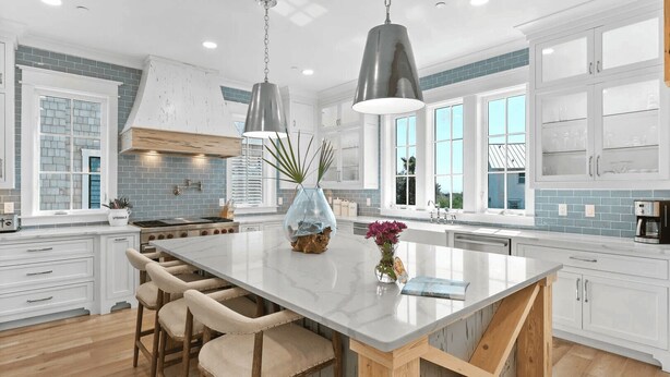 A spacious kitchen with a large island, white cabinetry, and a blue-tiled backsplash.