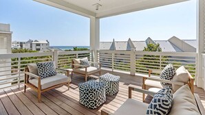 A covered outdoor seating area with wooden furniture and patterned cushions, overlooking a coastal view.