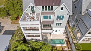 A multi-story house with a swimming pool, a deck with outdoor furniture, and a large window on the second floor.