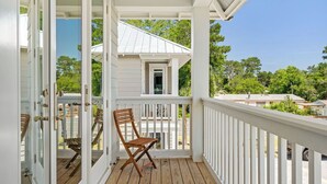 A wooden deck with a white railing, a folding chair, and a glass door leading to an outdoor area.