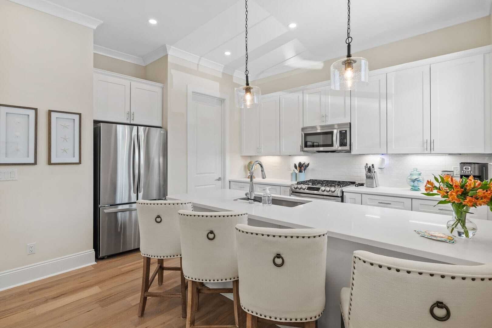 A modern kitchen with white cabinetry, stainless steel appliances, and a central island with bar stools.