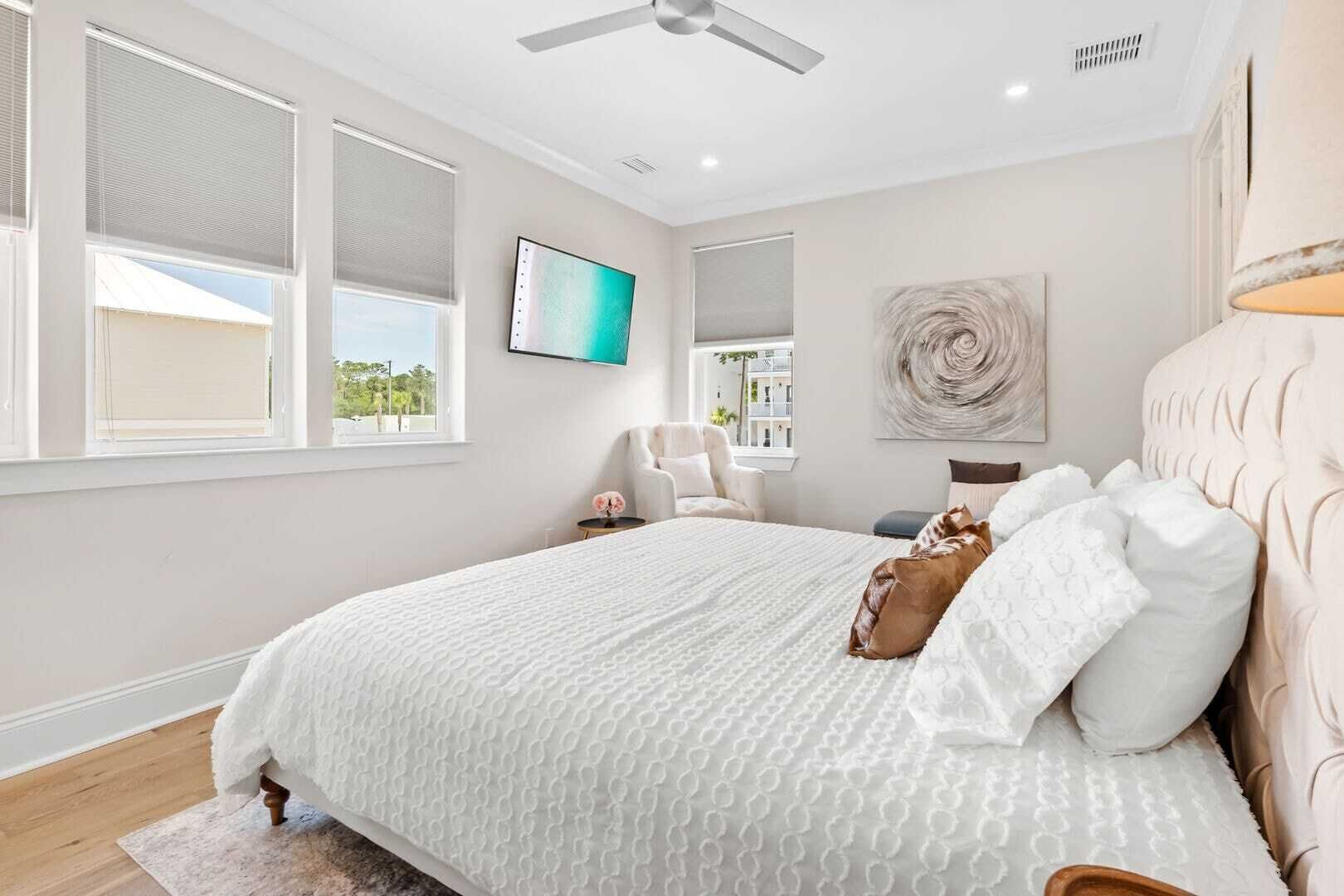 A bedroom with a large bed, a ceiling fan, and a TV on the wall.