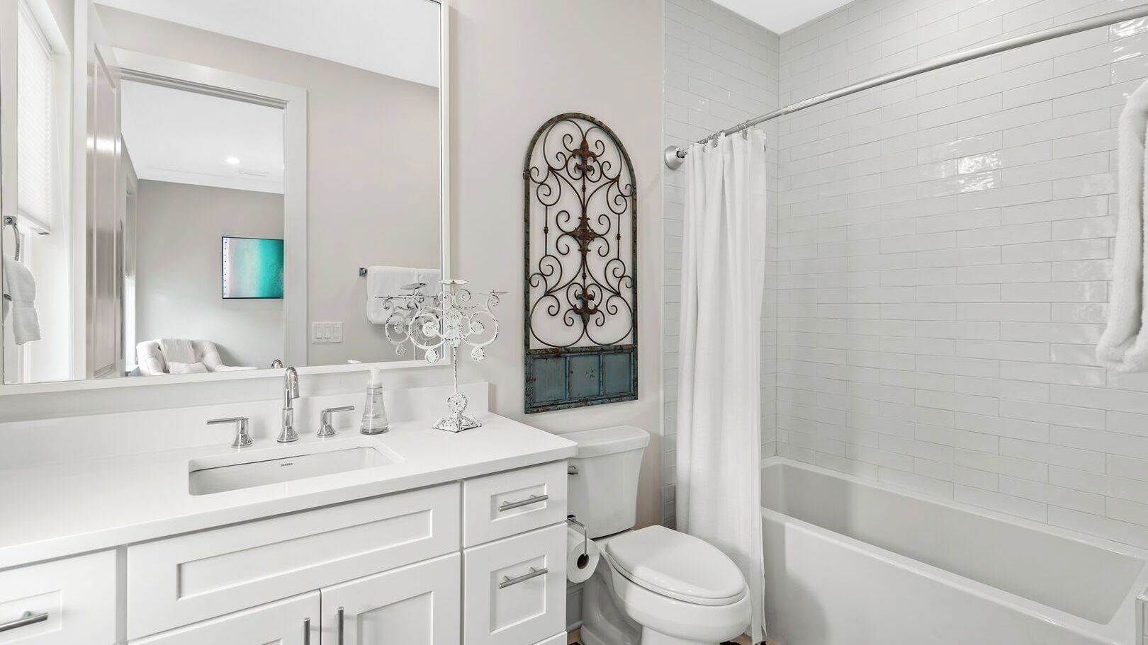Un baño moderno con un tocador blanco, inodoro, ducha y un detalle decorativo metálico sobre el inodoro.