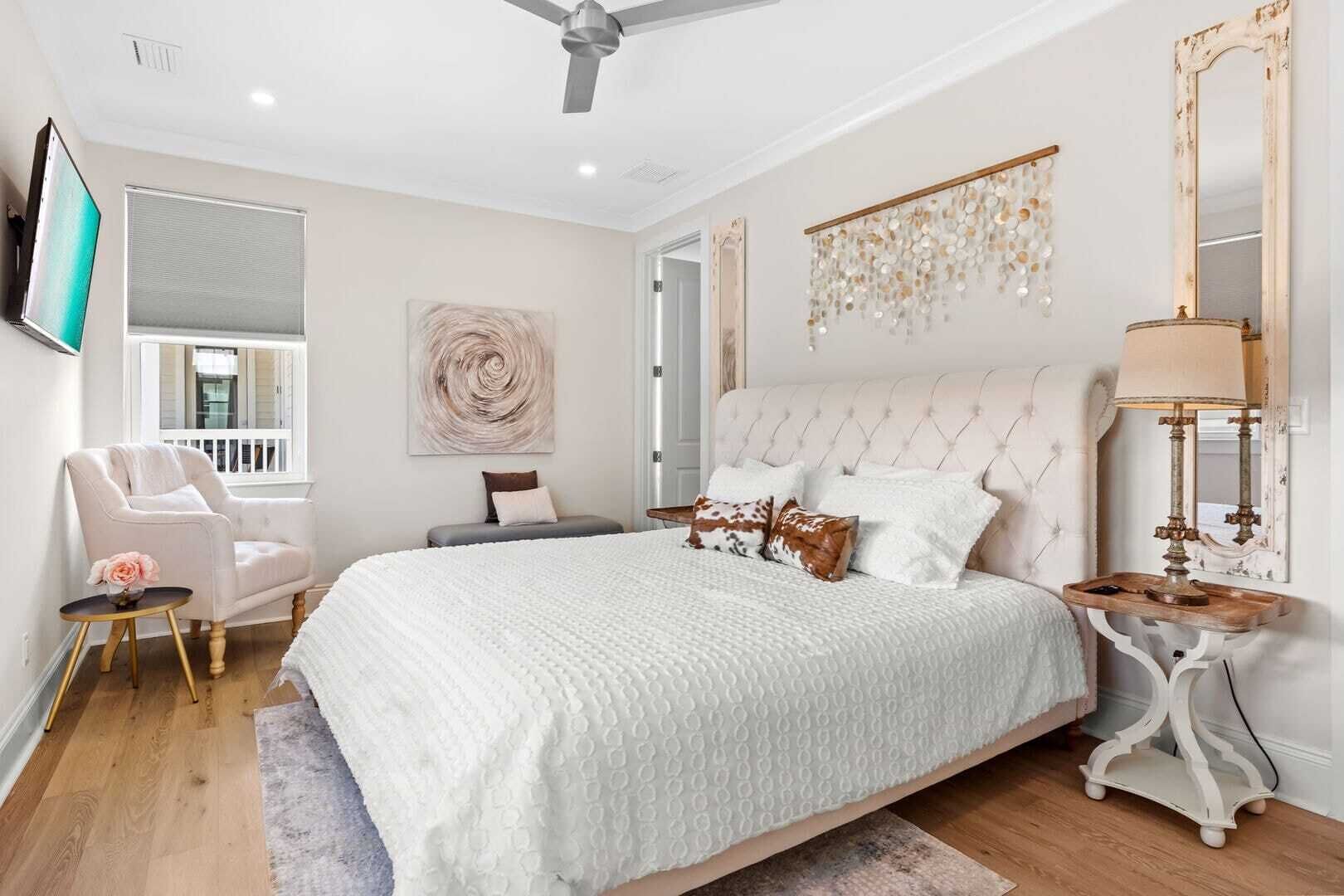A bedroom with a large bed, a chair, a small table, a lamp, and a mirror.