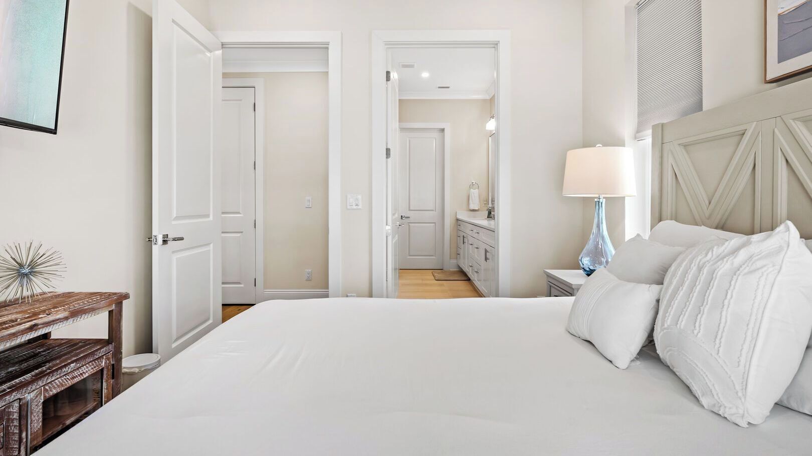 A hotel room with a large bed, a bedside table with a lamp, a wooden side table, and a mirror on the wall.