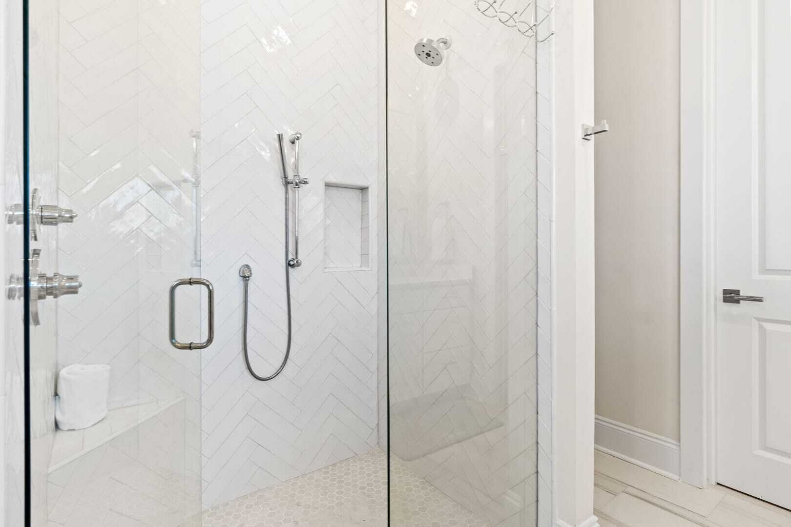 A glass-enclosed shower with a handheld showerhead and a wall-mounted faucet.