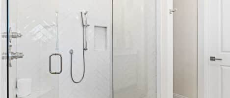 A glass-enclosed shower with a handheld showerhead and a wall-mounted faucet.