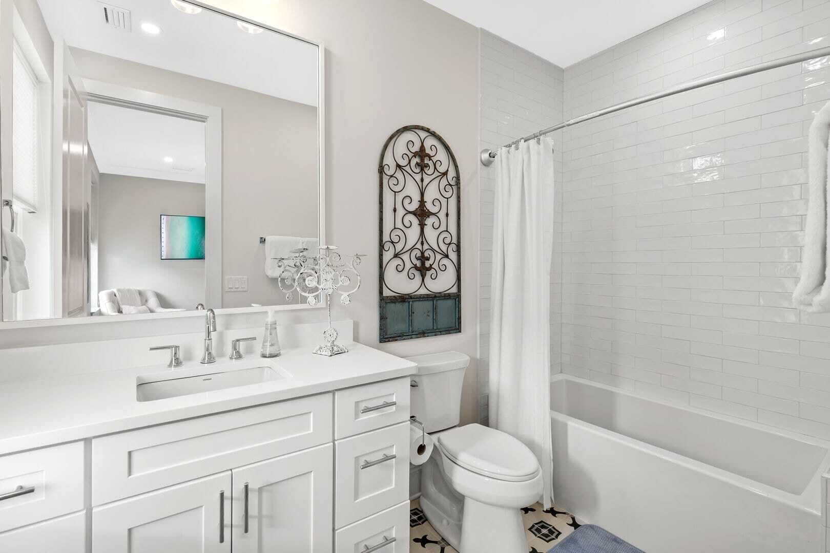 A modern bathroom with a white vanity, a large mirror, a decorative metal piece above the sink, and a shower area with a white curtain.