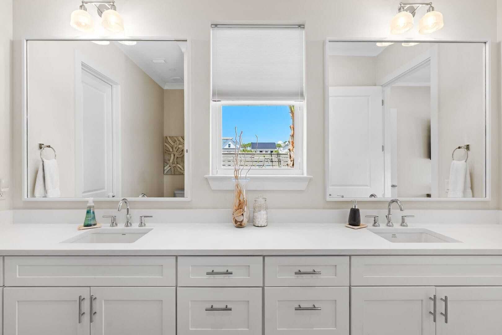 Une salle de bain avec deux lavabos, de grands miroirs et une fenêtre donnant sur des immeubles.
