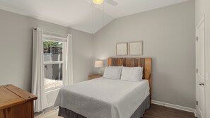 A bedroom with a bed, a nightstand, a wooden table, and a window with curtains.