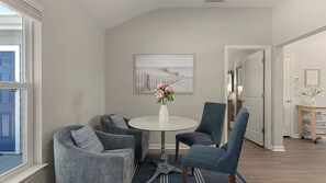 A room with a round table, two armchairs, a vase with flowers, a painting on the wall, and a door leading to another room. - Ocean Oasis by Avantstay Block to Beach West Pcb, Pet-friendly (Panama City Beach)