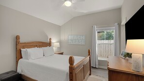 A bedroom with a wooden bed, a nightstand, a lamp, a framed picture, and a window with curtains. - Ocean Oasis by Avantstay Block to Beach West Pcb, Pet-friendly (Panama City Beach)