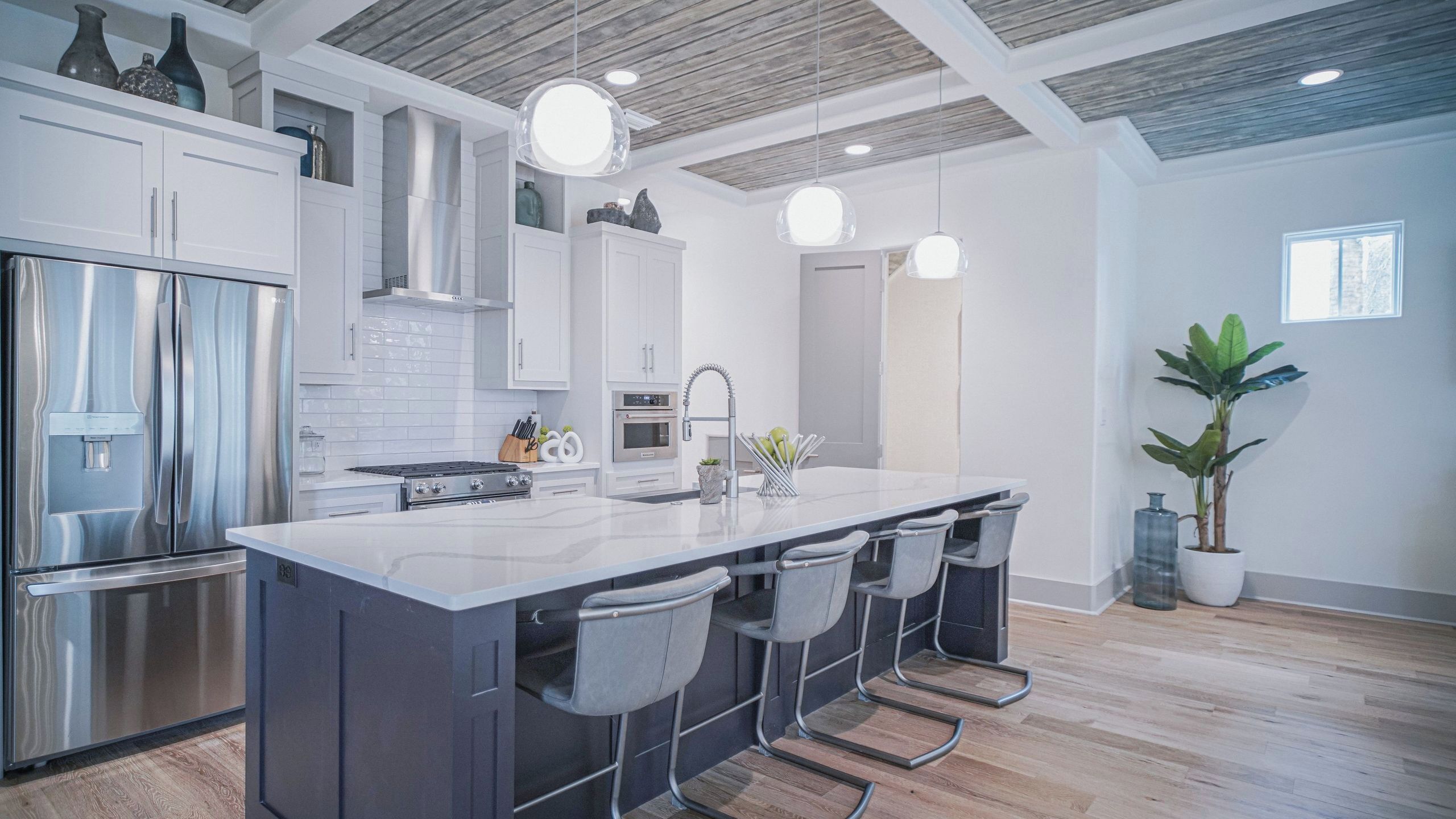 A modern kitchen with a central island, bar stools, stainless steel appliances, and pendant lighting.