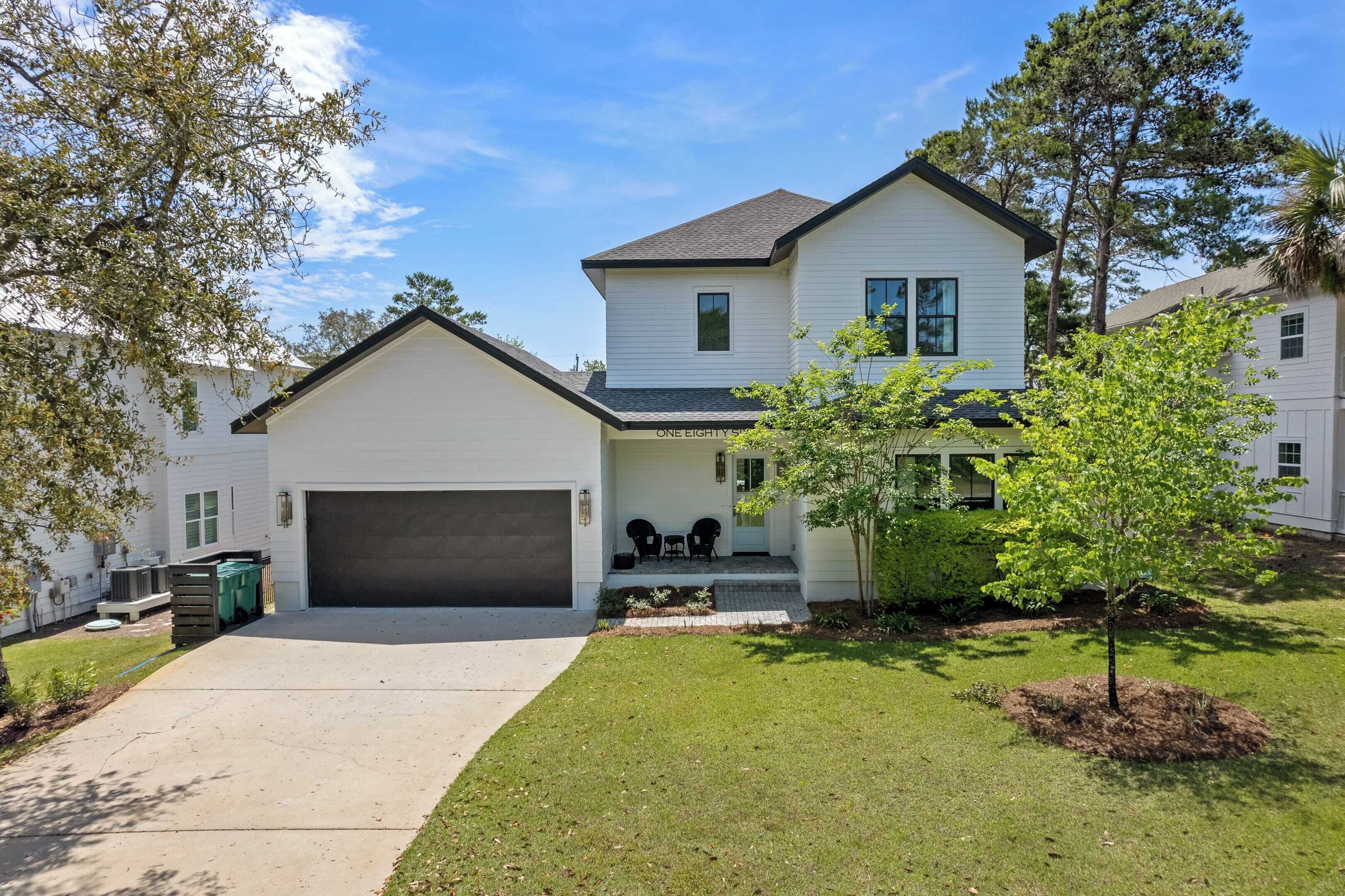 A two-story house with a garage, a small porch with chairs, and a well-maintained lawn.