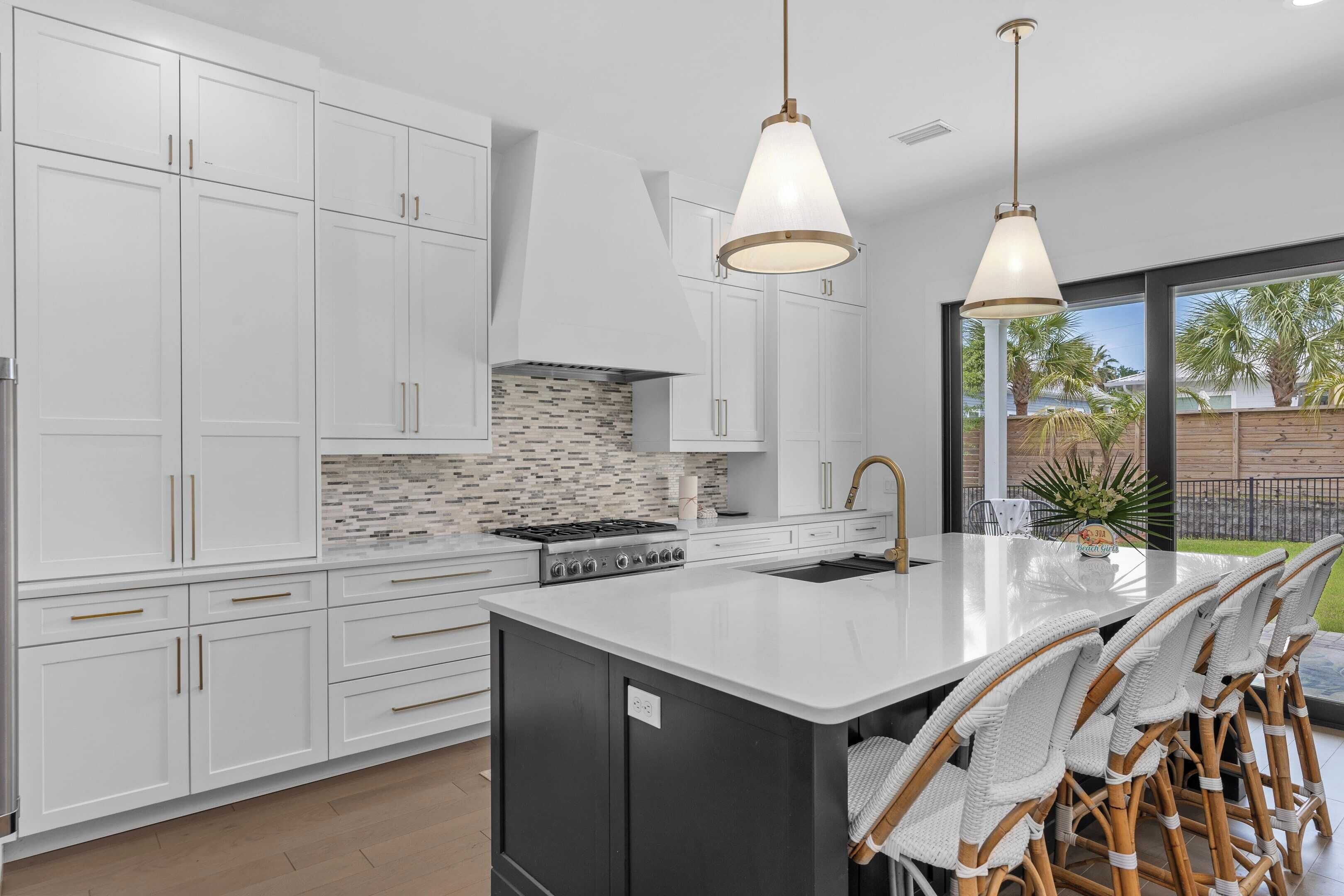 A modern kitchen with white cabinetry, a large island with bar stools, a gas stove, and pendant lighting.