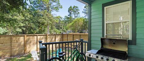 A patio with a grill, a bicycle, and a wooden fence.