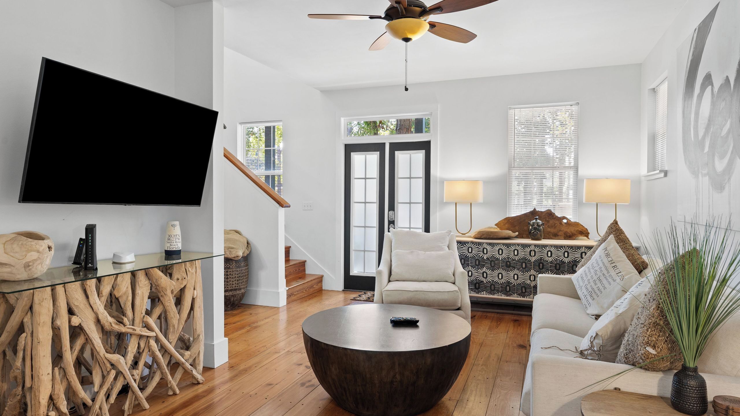 Un salon moderne avec un téléviseur à écran plat, une table basse ronde, un canapé, un fauteuil et un ventilateur de plafond.