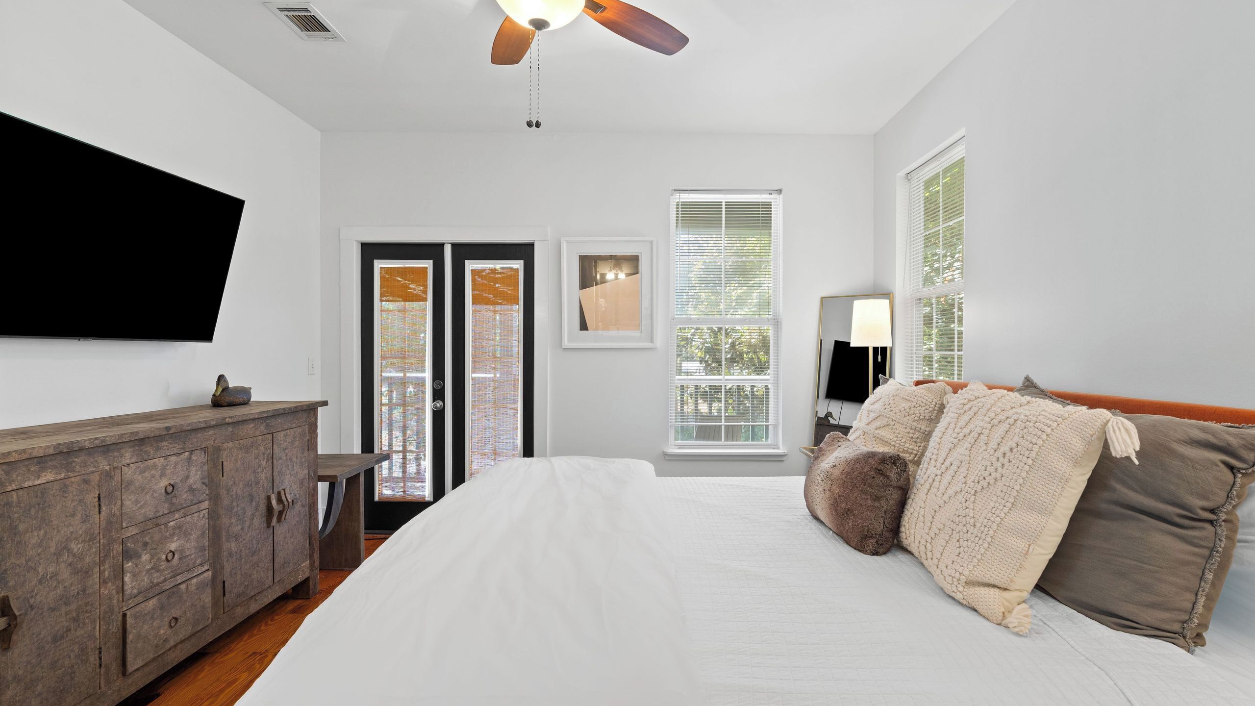 A bedroom with a bed, a wooden dresser, a ceiling fan, a TV, and a window with blinds.