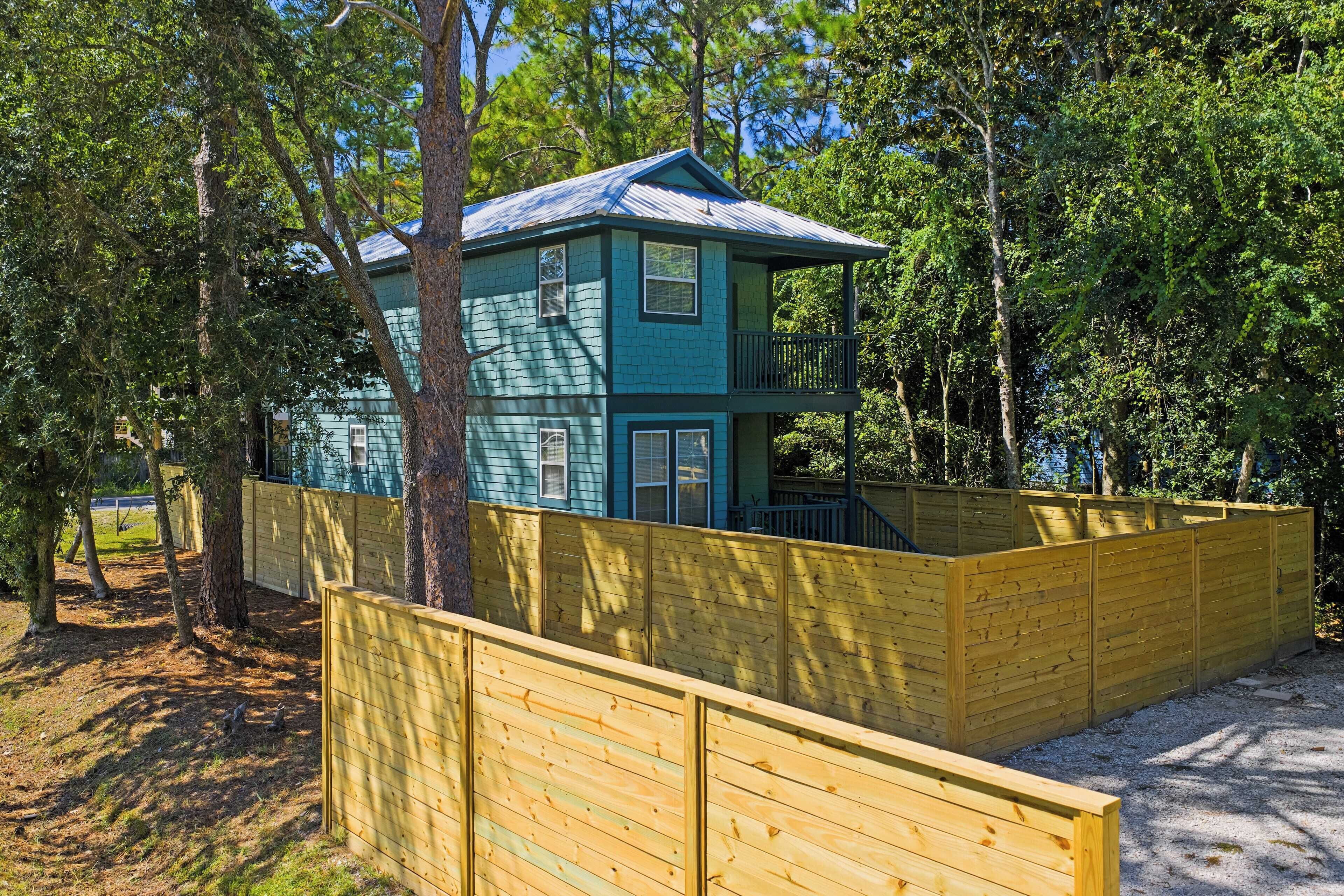 A two-story house with a balcony, surrounded by a wooden fence and trees.