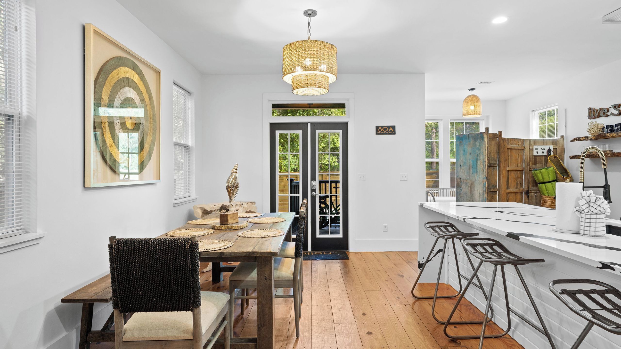 A modern kitchen with bar stools, a dining table with placemats, and a hanging light fixture.