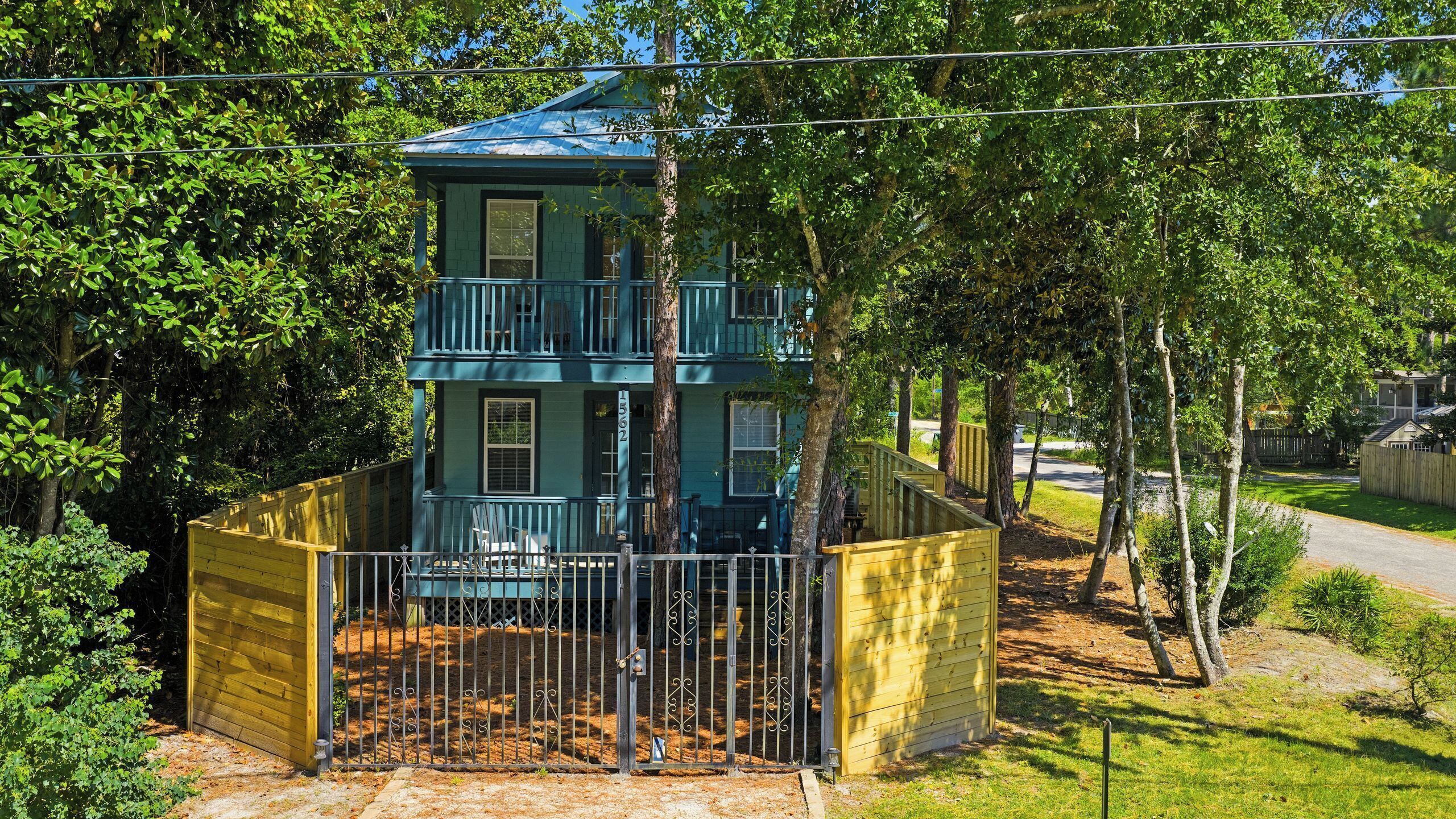 A two-story building with a balcony, surrounded by trees and a fenced yard.