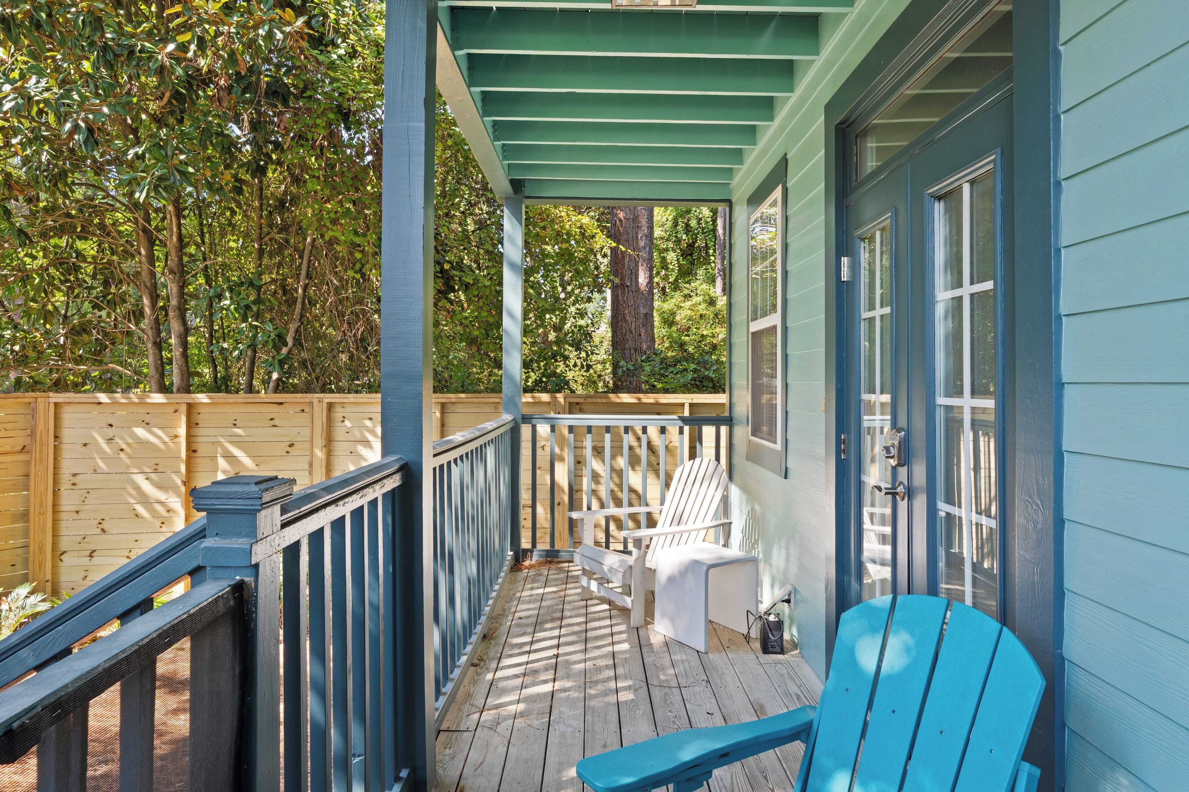 Eine überdachte Veranda mit einer Holzterrasse, einem weißen Adirondack-Sessel, einem blauen Adirondack-Sessel und einem Holzzaun.