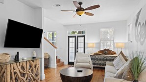 A modern living room with a flat-screen TV, a round coffee table, a sofa, and a ceiling fan. - Coastal Soul 393 by Avantstay Near Boat Ramp & Bay, Private Yard (Santa Rosa Beach)