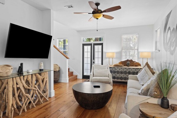A modern living room with a flat-screen TV, a round coffee table, a sofa, and a ceiling fan. - Coastal Soul 393 by Avantstay Near Boat Ramp & Bay, Private Yard (Santa Rosa Beach)