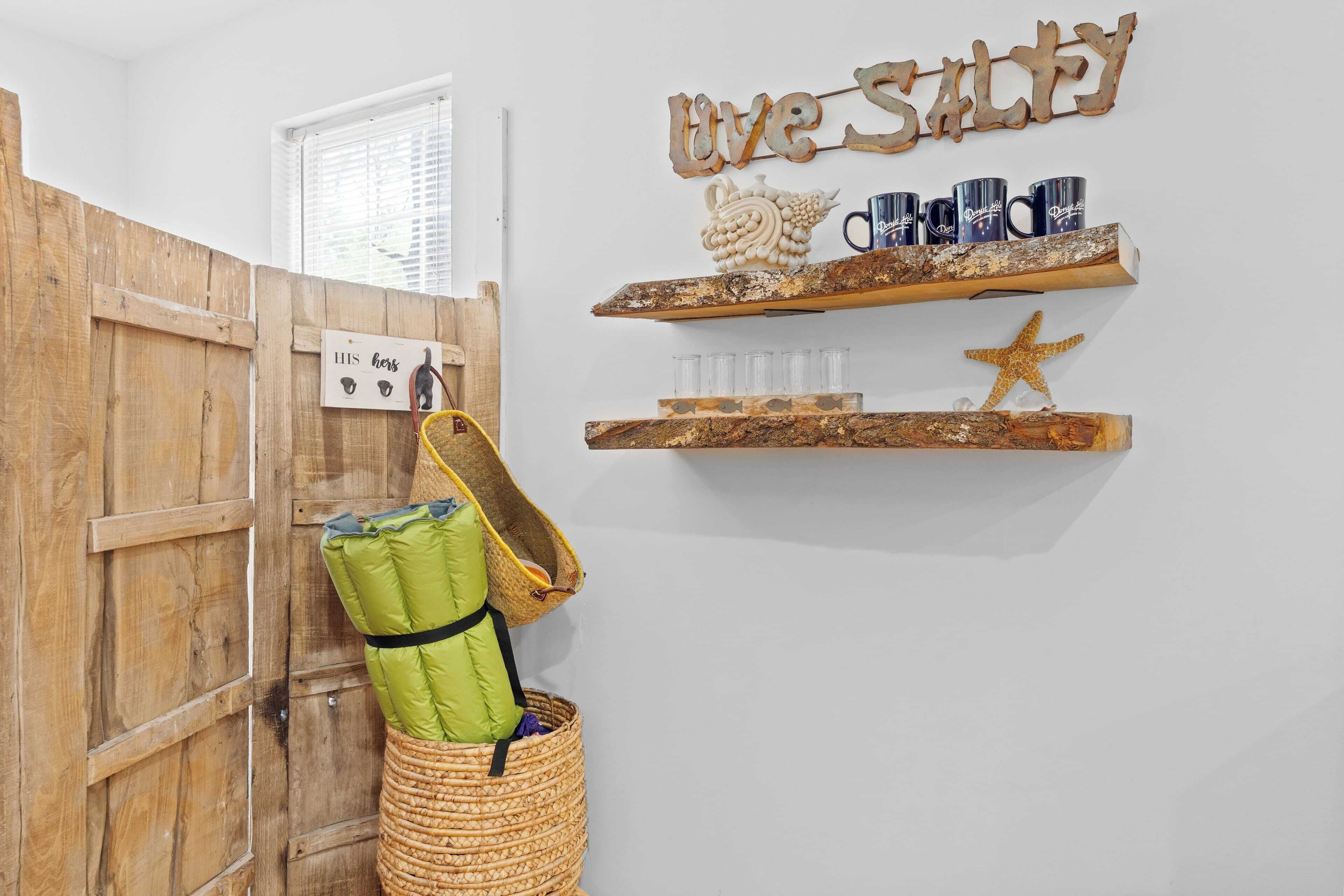 A room with a wooden door, a wicker basket, a shelf with mugs, and a sign that reads "Live Salty".