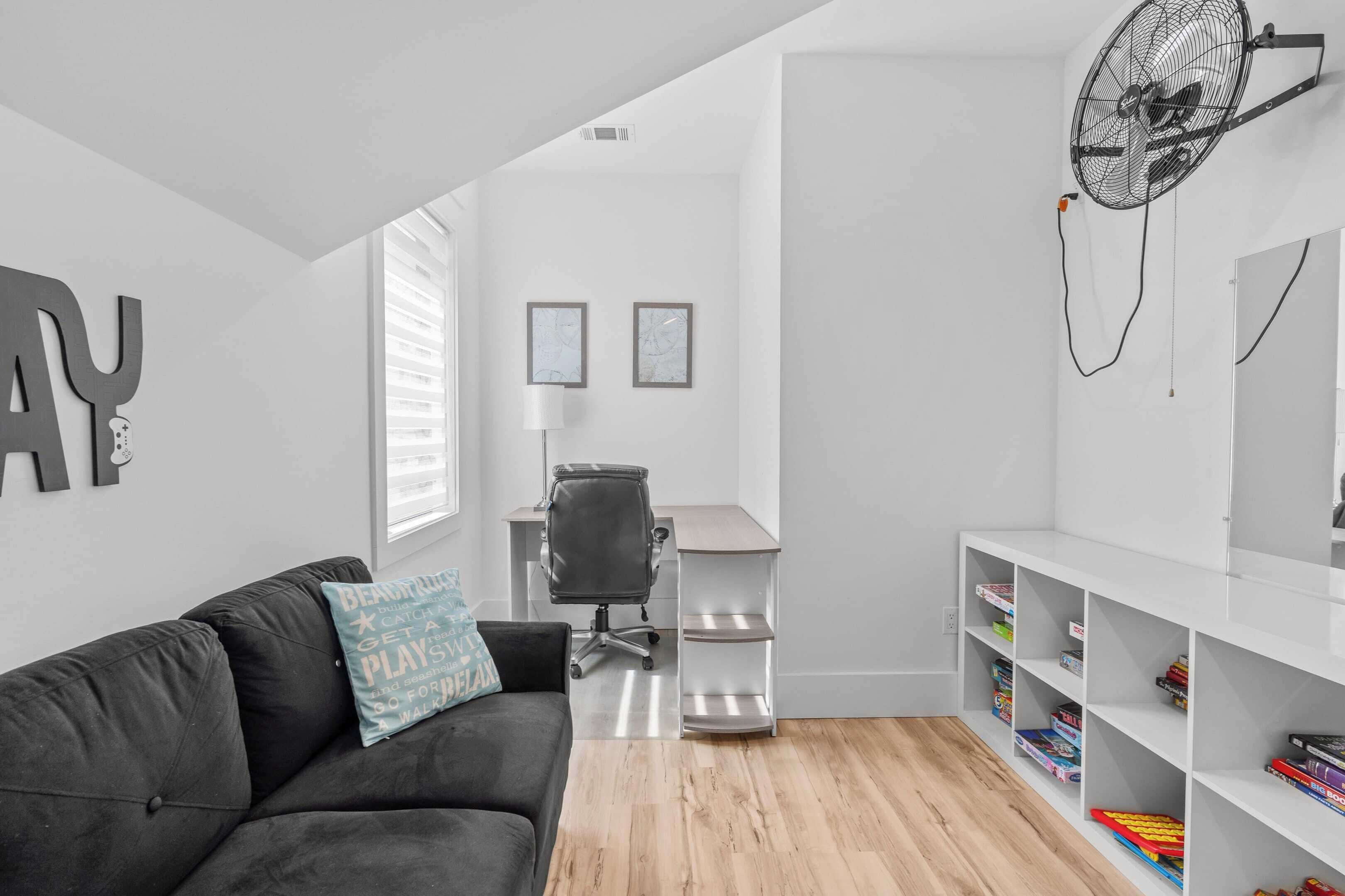 A modern, minimalistic room with a grey sofa, a desk, and a bookshelf.