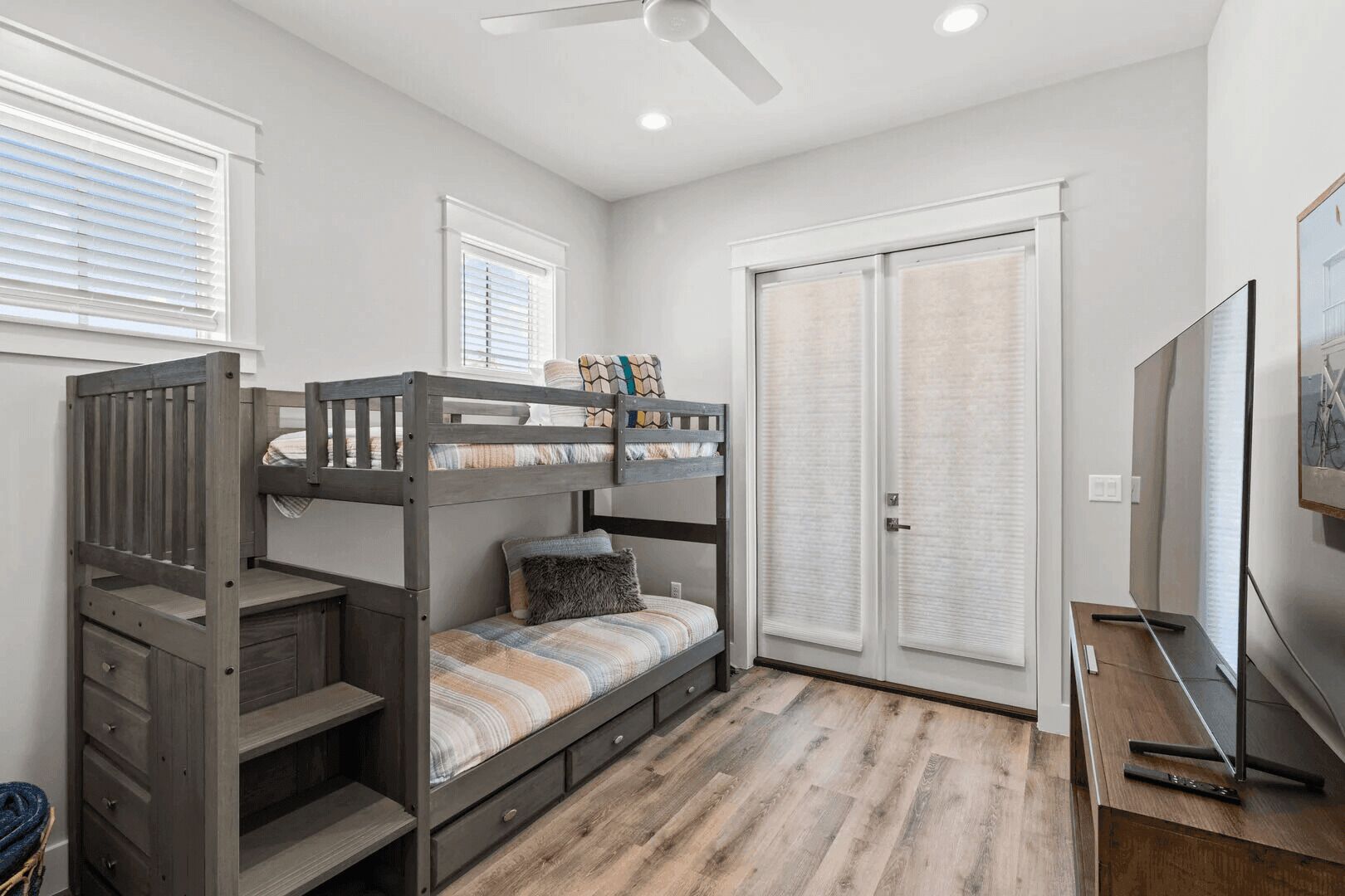 A bunk bed with drawers, a ceiling fan, and a TV.