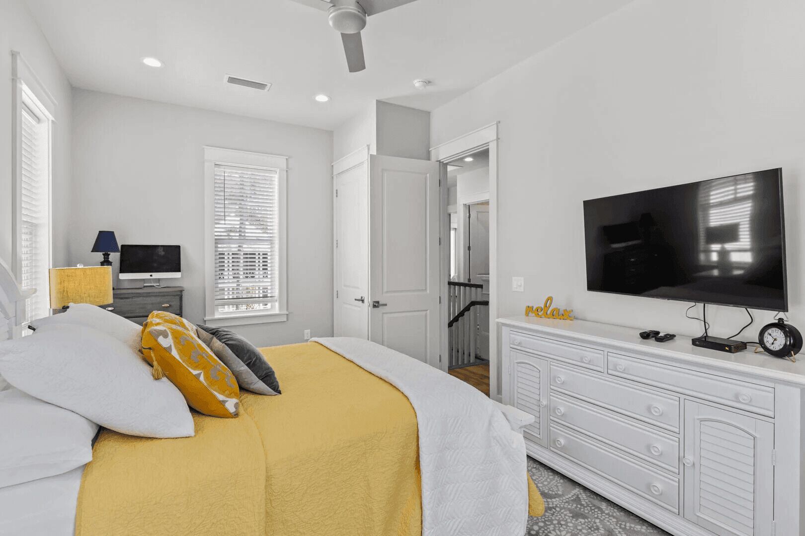 A bedroom with a bed, a TV, a dresser, and a door leading to another room.