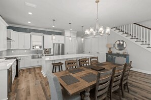 Una cocina moderna con armarios blancos, un refrigerador de acero inoxidable, una isla grande con taburetes de bar y una mesa de comedor de madera.