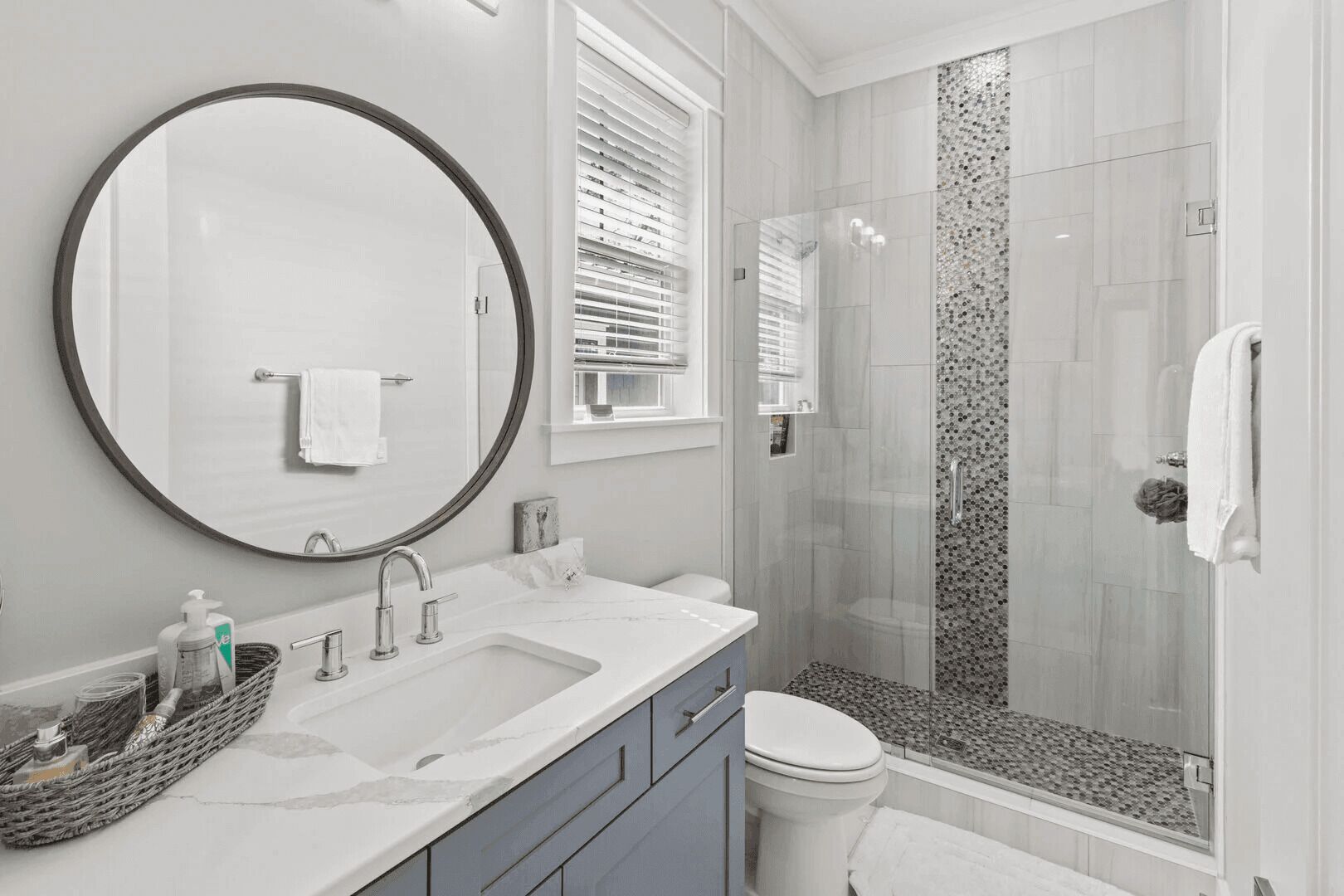 Een moderne badkamer met een grote ronde spiegel, twee wastafels, een toilet en een douche met glazen wand.